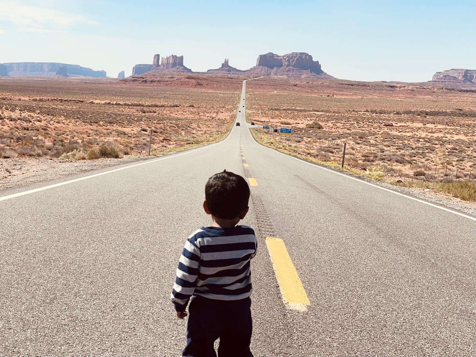 Child standing on Highway 163 facing monument valley during a Utah road trip with kids