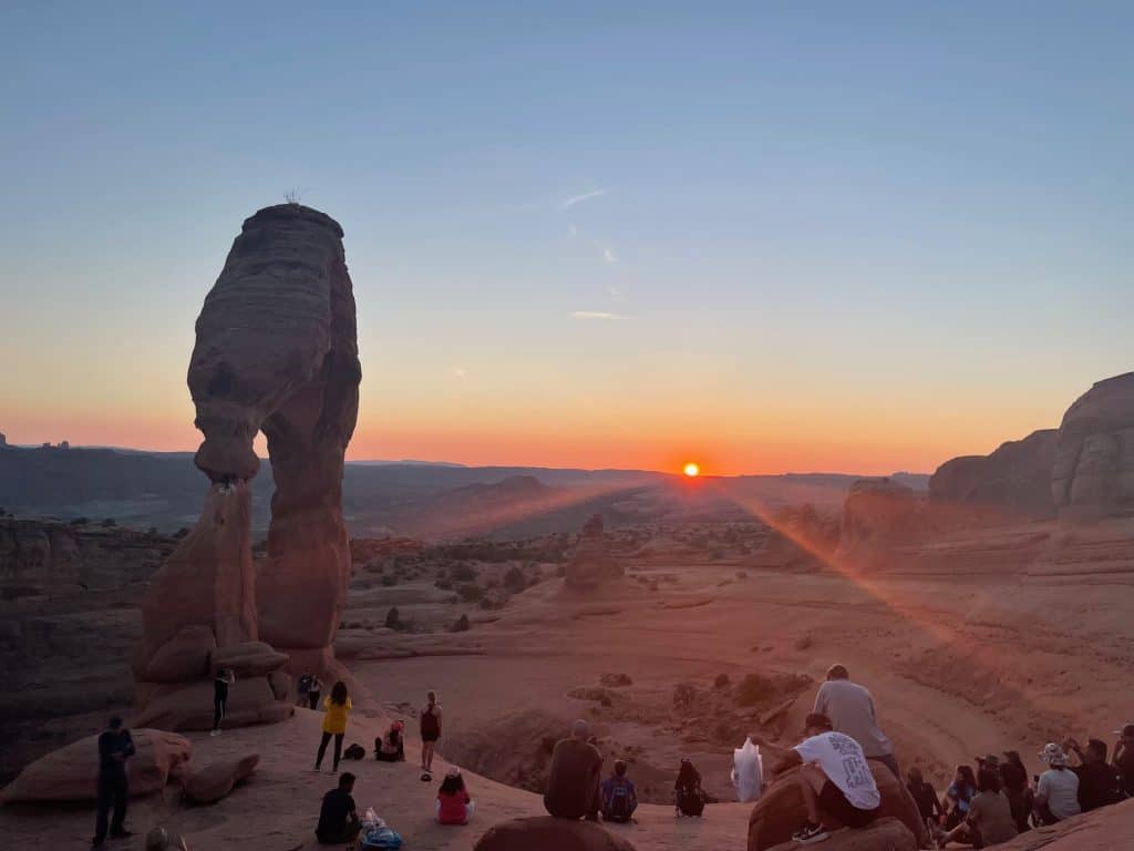 Delicate Arch at sunset with families sitting on the rocks.